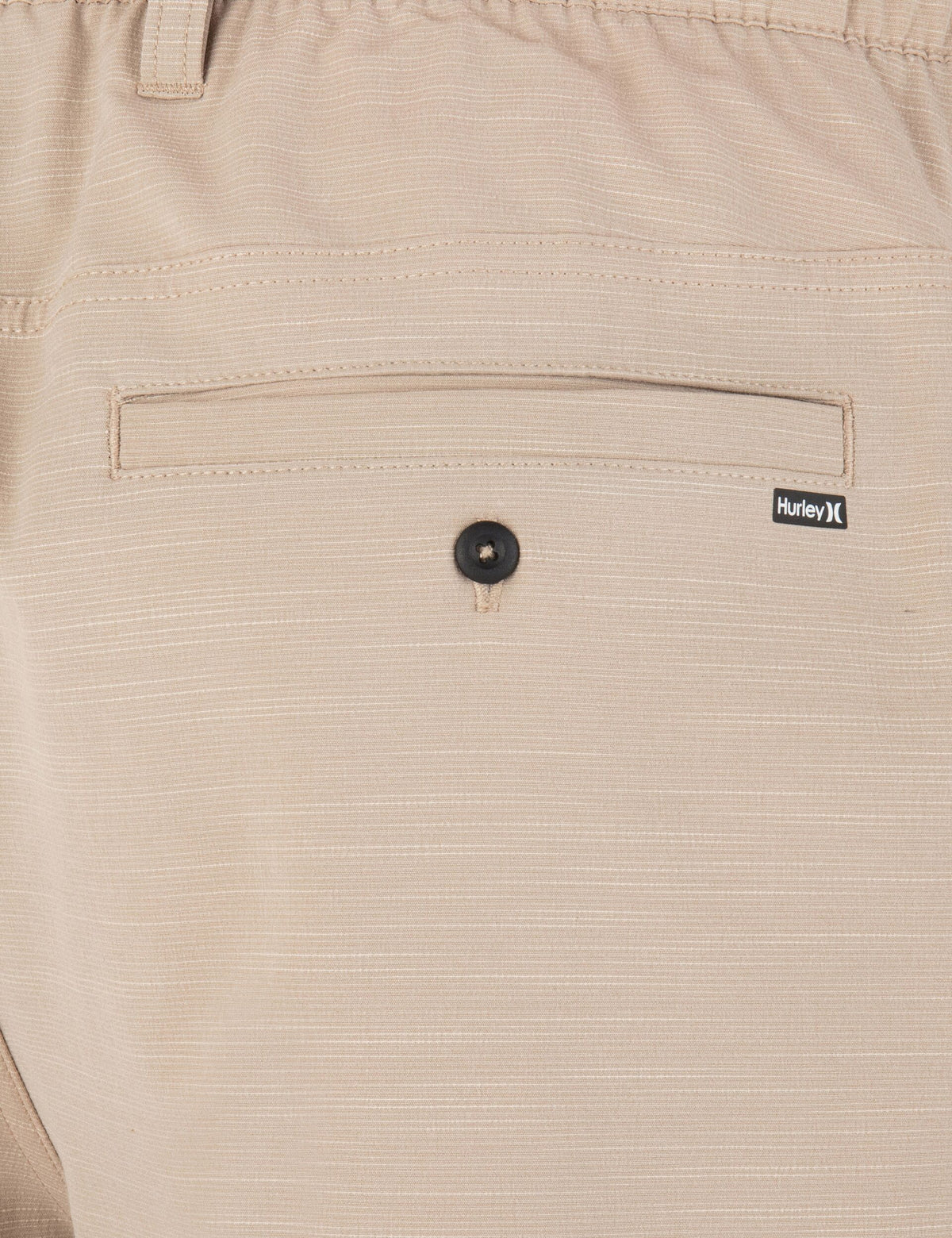 Close-up of beige pants with a button and Hurley logo on the pocket.