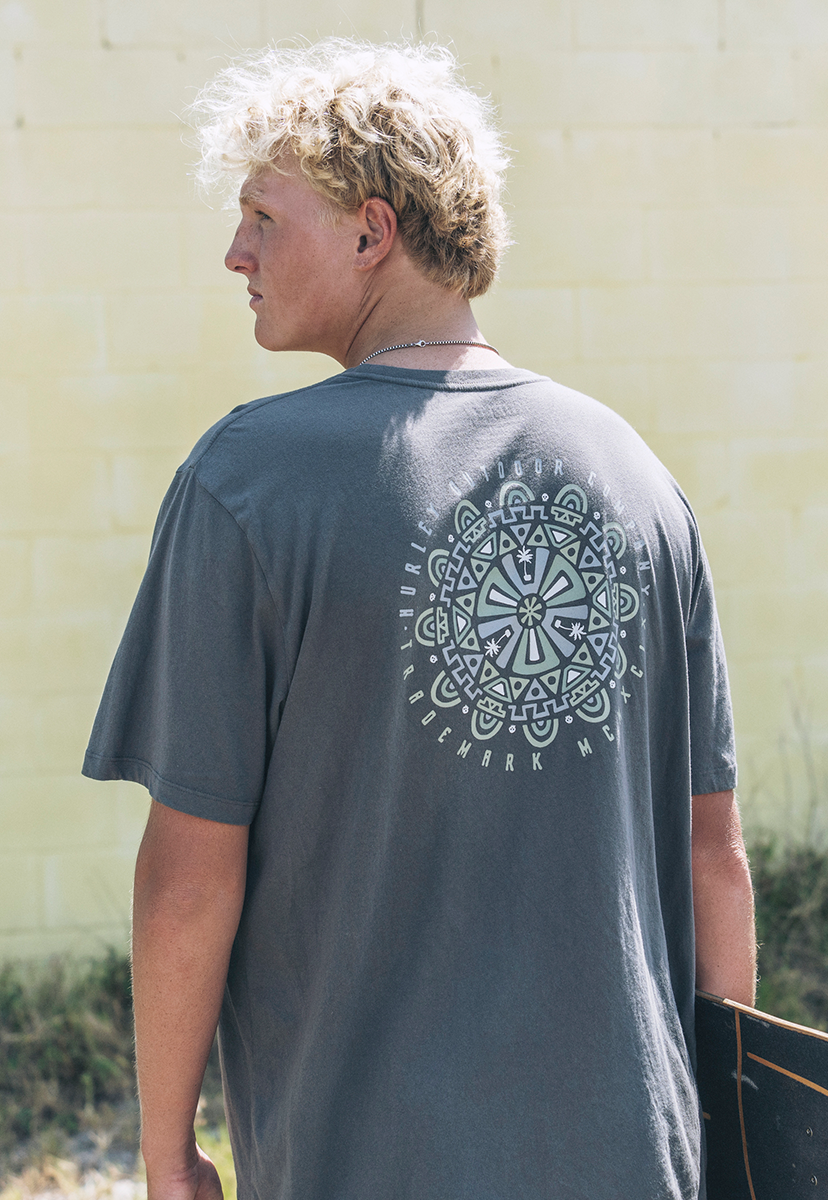 Person wearing a gray t-shirt with a white geometric design on the back, standing against a light-colored wall.