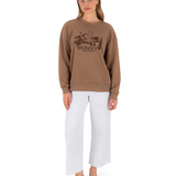 Woman wearing a brown sweatshirt with a logo and text, standing against a white background