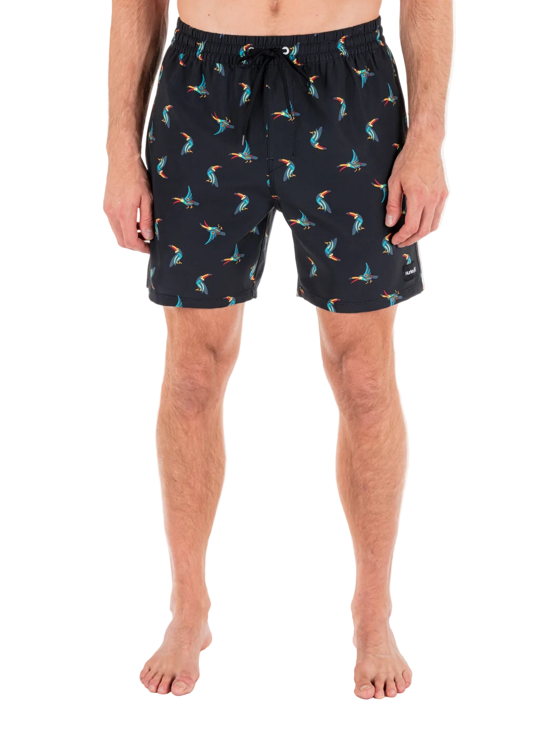 Person wearing black swim shorts with colorful parrot pattern on a white background