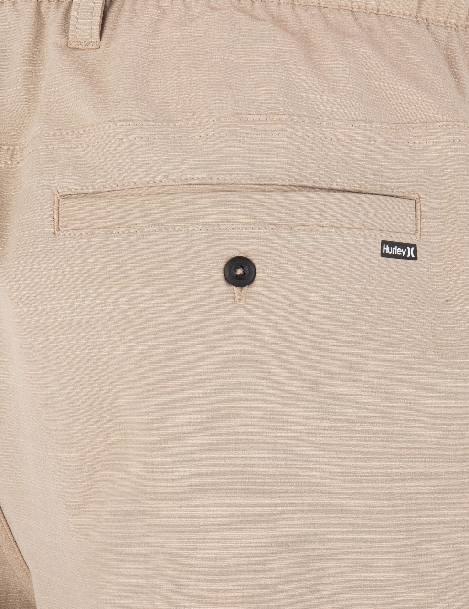 Close-up of beige pants with a button and Hurley logo on the pocket.